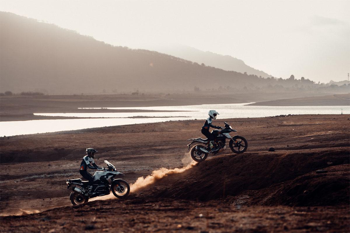 Two riders kicking up dust on a trail beside the reservoir